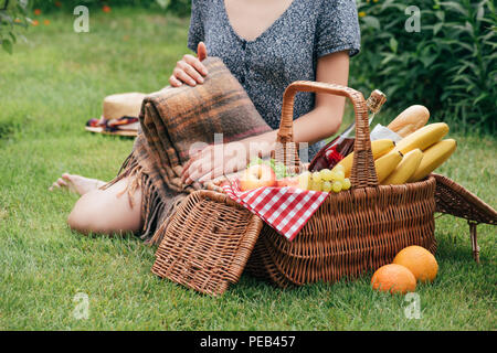 Zugeschnittenes Bild der Frau mit Decke und sitzen auf grünem Gras an Picknick im Park Stockfoto