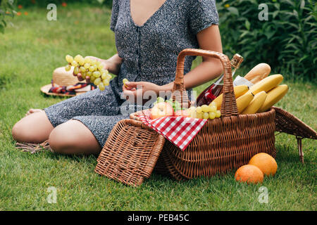 7/8 Bild der Frau Trauben essen und sitzen auf grünem Gras im Picnic Stockfoto