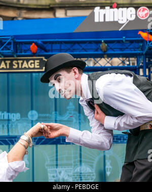 Edinburgh, Schottland, Großbritannien. 14. August 2018. Edinburgh Fringe Festival Street Performer, Royal Mile, Edinburgh, Schottland, Vereinigtes Königreich. Charlie Chaplin clown Imitator auf Stelzen beugte die Hand einer Frau zu küssen. Stockfoto