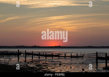 Gerade die Sonne über dem Horizont verschwinden von Seasalter Strand genommen, Kent, UK auf der Insel Sheppey. Das alte Meer Abwehr sind sichtbar. Stockfoto