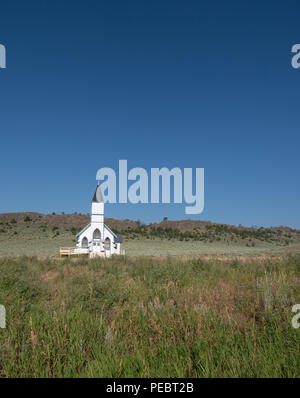 Die alte Weiße Schindeln Trinity Lutheran Church in Lennep Montana mit Hügeln, Salbei Pinsel und blauen Himmel im Hintergrund. Stockfoto