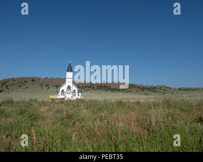 Die alte Weiße Schindeln Trinity Lutheran Church in Lennep Montana mit Hügeln, Salbei Pinsel und blauen Himmel im Hintergrund. Stockfoto