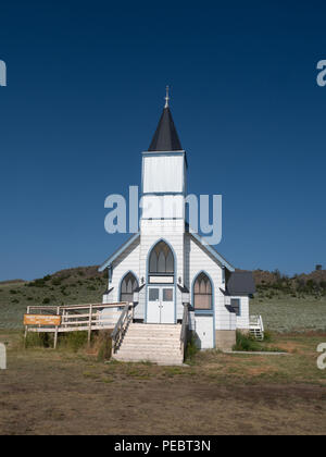 Die alte Weiße Schindeln Trinity Lutheran Church in Lennep Montana mit Hügeln, Salbei Pinsel und blauen Himmel im Hintergrund. Stockfoto