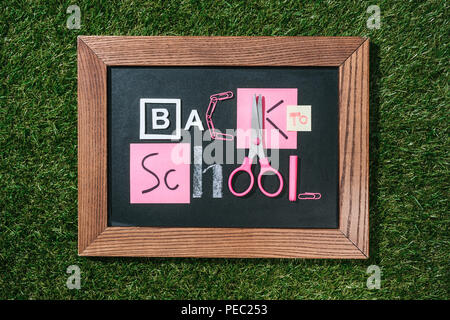 Blick von oben auf die Tafel mit zurück in die Schule Schriftzug aus rosa und weiße Objekte auf grünen Rasen Stockfoto