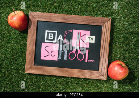 Blick von oben auf die frische Äpfel und Tafel mit zurück in die Schule Schriftzug aus rosa und weiße Objekte auf grünen Rasen Stockfoto