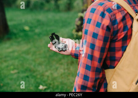 7/8 Schuß des jungen Mannes in kariertem Hemd holding Kompass im Wald Stockfoto