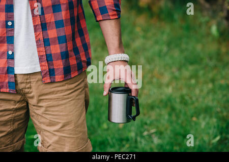 Teilansicht des Menschen in kariertem Hemd holding Becher im Freien Stockfoto