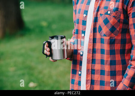 7/8 Schuß des jungen Mannes in kariertem Hemd holding Becher im Freien Stockfoto