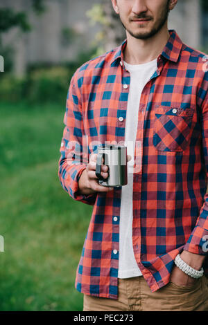 7/8 Schuß des jungen Mannes in kariertem Hemd holding Becher Stockfoto