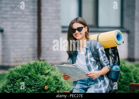 Glückliche junge Frau mit Rucksack, Karte und lächelnd an Kamera Stockfoto