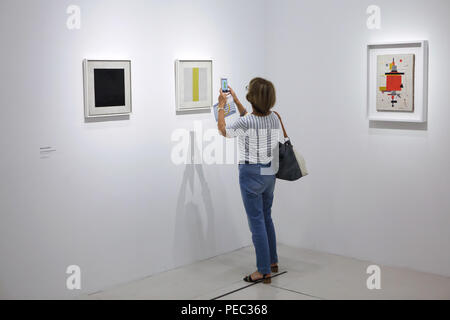 Besucher auf einem Smartphone das Gemälde Bild der russischen Avantgarde Avantgarde Maler Nikolai Suetin "Komposition mit einem gelben Streifen" aus dem Jahr 1920 datiert wird in der Ausstellung im Centre Pompidou in Paris, Frankreich angezeigt. Gemälde von Nikolai Suetin 'Zusammensetzung' (1920) an der rechten und "Schwarzes Quadrat" (1920er Jahre) Links, welche eine Kopie nach dem berühmten Gemälde von Russischen Avantgarde Maler Kasimir Malewitsch, sind in dem Bild zu sehen. Die Ausstellung der russischen Avantgarde gewidmet - Garde in Witebsk (1918-1922) läuft bis 16. Juli 2018. Stockfoto