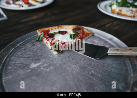 Scheibe der leckere Pizza mit Server auf Wanne aus Metall und Holz Tisch Stockfoto