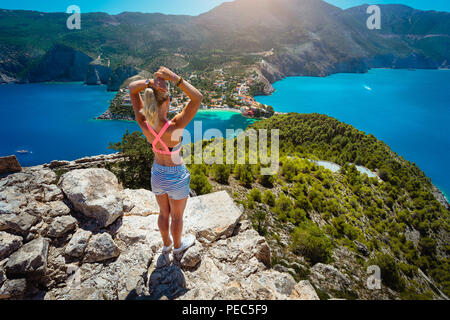 Junge Frauen mit Blick auf das Dorf Assos Kefalonia von oben Schloss. Schöne Blaue Lagune unterhalb von Pinien und Zypressen umgeben. Hals Land verbinden Festland. Griechenland Stockfoto