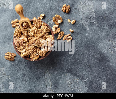 Walnusskerne mit Holz- Schaufel auf grauem Hintergrund mit kopieren. Muttern in Ton Schüssel. Ansicht von oben. Stockfoto