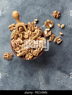 Walnusskerne mit Holz- Schaufel auf grauem Hintergrund mit kopieren. Muttern in Ton Schüssel. Ansicht von oben. Stockfoto