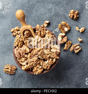 Walnusskerne mit Holz- Schaufel auf grauen Hintergrund. Muttern in Ton Schüssel. Ansicht von oben. Stockfoto