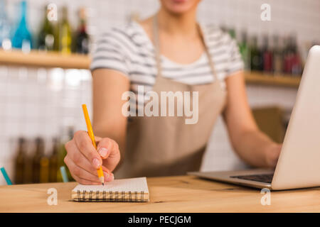 Für die Arbeit. Noten, die durch eine schöne angenehme junge Frau getroffen werden, während sie an der Theke im Cafe stehend Stockfoto