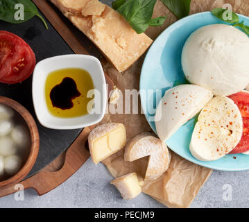 Italienische Käsesorten. Mozzarella Büffel, crottin, Bälle, Stracciatella, Basilikum, Tomaten, Olivenöl und Essig auf grauem Hintergrund. Ansicht von oben, kopieren. Stockfoto