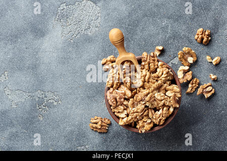 Walnusskerne mit Holz- Schaufel auf grauem Hintergrund mit kopieren. Muttern in Ton Schüssel. Ansicht von oben. Stockfoto