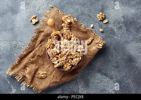Walnusskerne hölzerne Schaufel auf grauem Hintergrund mit kopieren. Muttern in Ton Schüssel. Ansicht von oben. Stockfoto