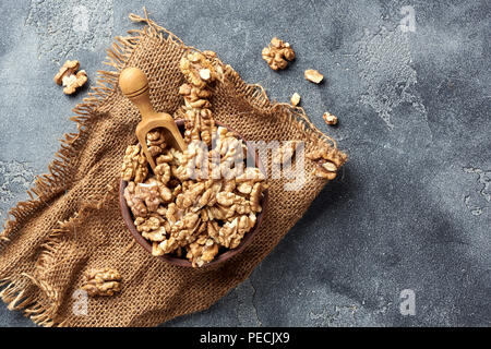 Walnusskerne hölzerne Schaufel auf grauem Hintergrund mit kopieren. Muttern in Ton Schüssel. Ansicht von oben. Stockfoto