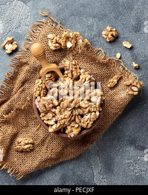 Walnusskerne hölzerne Schaufel auf grauem Hintergrund mit kopieren. Muttern in Ton Schüssel. Ansicht von oben. Stockfoto