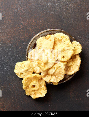 Getrocknete kandierte Ananas Ringe. Süße Früchte in Scheiben geschnitten auf Braun konkreten Hintergrund. Ansicht von oben. Stockfoto