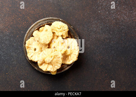 Getrocknete kandierte Ananas Ringe. Süße Früchte in Scheiben geschnitten auf Braun konkreten Hintergrund. Ansicht von oben. Stockfoto