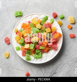 Würfel von getrockneten Aprikosen, Kiwi, Mango, Ananas und Papaya auf weiße Platte. Kandierte Früchte über grauen Hintergrund. Ansicht von oben. Stockfoto