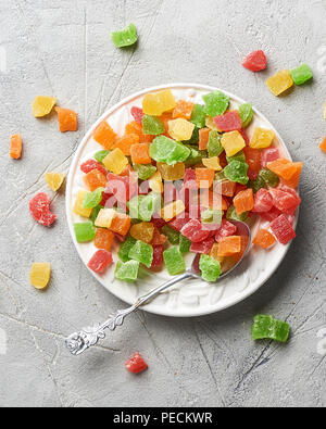 Würfel von getrockneten Aprikosen, Kiwi, Mango, Ananas und Papaya auf weiße Platte. Kandierte Früchte über grauen Hintergrund. Ansicht von oben. Stockfoto