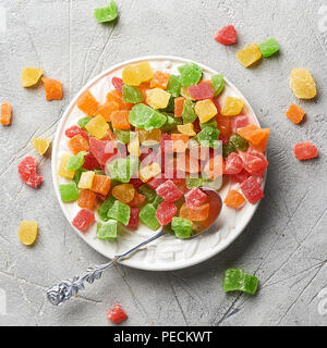 Würfel von getrockneten Aprikosen, Kiwi, Mango, Ananas und Papaya auf weiße Platte. Kandierte Früchte über grauen Hintergrund. Ansicht von oben. Stockfoto