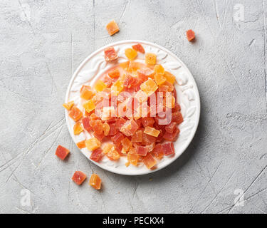 Würfel von getrockneten Aprikosen, Mangos und Papayas auf weiße Platte. Kandierte Früchte über grauer Hintergrund mit kopieren. Ansicht von oben. Stockfoto