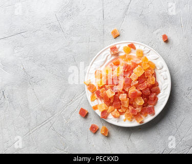 Würfel von getrockneten Aprikosen, Mangos und Papayas auf weiße Platte. Kandierte Früchte über grauer Hintergrund mit kopieren. Ansicht von oben. Stockfoto