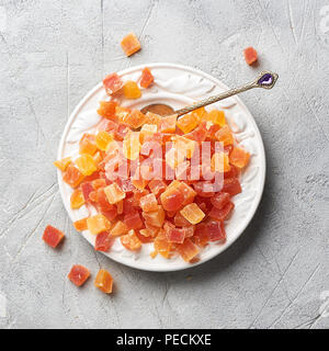 Würfel von getrockneten Aprikosen, Mangos und Papayas auf weiße Platte. Kandierte Früchte über grauen Hintergrund. Ansicht von oben. Stockfoto