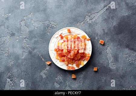 Würfel von getrockneten Aprikosen, Mangos und Papayas auf weiß palte. Kandierte Früchte über grauer Hintergrund mit kopieren. Ansicht von oben. Stockfoto