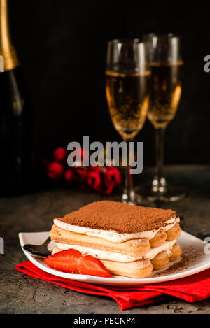 Tiramisu mit Erdbeeren und Gläser Champagner auf dem Tisch. Valentines Konzept. Dunkle moody Stil. Stockfoto