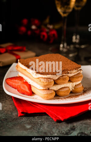 Tiramisu mit Erdbeeren und Gläser Champagner auf dem Tisch. Valentines Konzept. Dunkle moody Stil. Stockfoto