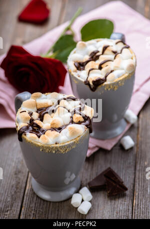 S'mores trinken. Zwei Becher heißer Schokolade mit Marshmallows auf einem Holztisch. Kakao. Rosenblätter. Valentine. Stockfoto