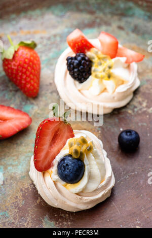 Mini Pavlova baiser Kuchen mit Beeren und Passionsfrüchte auf rustikalen vintage Hintergrund. Ansicht von oben. Stockfoto
