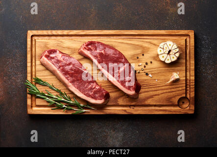 Rohe frische Fleisch Picanha Steak, traditionelle brasilianische Schnitt mit Rosmarin und Knoblauch und schwarzen Pfeffer auf Holzbrett. Geschnetzeltes Fleisch Steaks. Ansicht von oben. Stockfoto