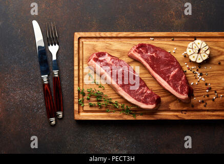 Rohe frische Fleisch Picanha Steak, traditionelle brasilianische Schnitt mit Rosmarin, Knoblauch, Messer und schwarzer Pfeffer auf Holzbrett. Geschnetzeltes Fleisch Steaks. Ansicht von oben. Stockfoto