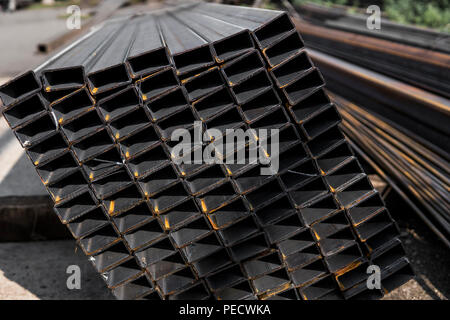Square flat-rolled pipe metal profile in packs at the warehouse of metal products. Weathered metals profiles for construction. Metal corrosion Stockfoto
