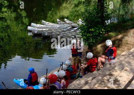 Kinder sitzen auf Schritte, Schwimmwesten und Helme auf der Bank des Wye River warten auf Kanu Unterricht Symonds Yat Stockfoto