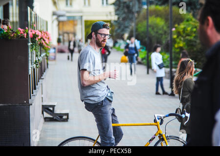 September 22, 2018 Minsk, Weißrussland: Junger Mann stand mit gelben fixie Bike im Stadtbild und macht Hand-roll Zigarette Stockfoto