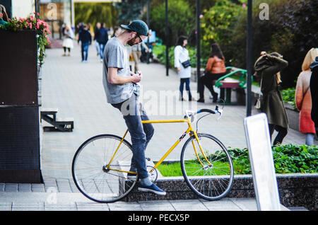 September 22, 2018 Minsk, Weißrussland: Junger Mann stand mit gelben fixie Bike im Stadtbild und macht Hand-roll Zigarette Stockfoto