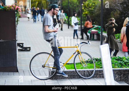 September 22, 2018 Minsk, Weißrussland: Junger Mann stand mit gelben fixie Bike im Stadtbild und macht Hand-roll Zigarette Stockfoto