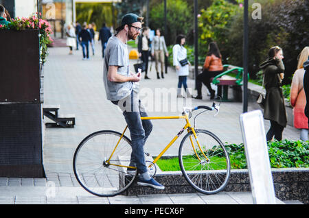 September 22, 2018 Minsk, Weißrussland: Junger Mann stand mit gelben fixie Bike im Stadtbild und macht Hand-roll Zigarette Stockfoto