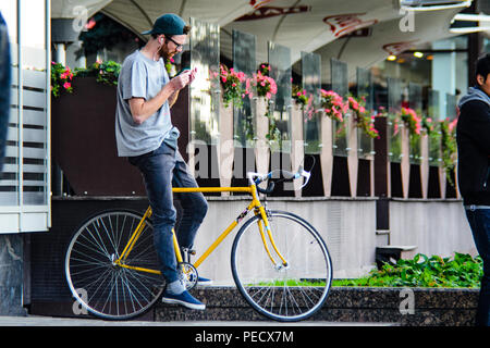 September 22, 2018 Minsk, Weißrussland: Junger Mann stand mit gelben fixie Bike im Stadtbild und macht Hand-roll Zigarette Stockfoto