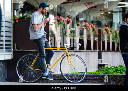 September 22, 2018 Minsk, Weißrussland: Junger Mann stand mit gelben fixie Bike im Stadtbild und macht Hand-roll Zigarette Stockfoto