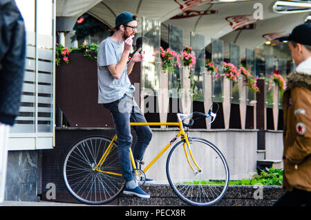 September 22, 2018 Minsk, Weißrussland: Junger Mann stand mit gelben fixie Bike im Stadtbild und macht Hand-roll Zigarette Stockfoto